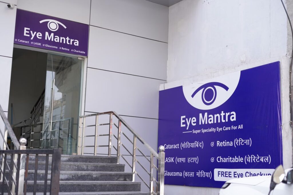 Front entrance of Eye Mantra Hospital Bahadurgarh showing staircase and banner with services like LASIK, cataract, glaucoma, retina, and free eye checkup.