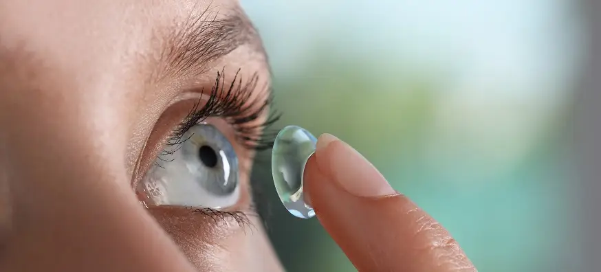 Close-up of a person inserting a contact lens into their eye, highlighting vision correction and contact lens usage.