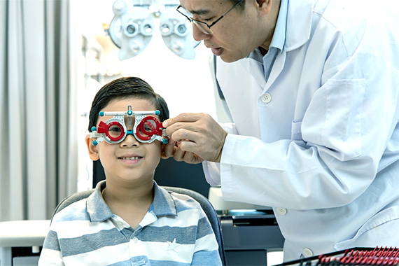 Eye doctor performing vision test for nearsightedness in a young boy using a trial lens frame