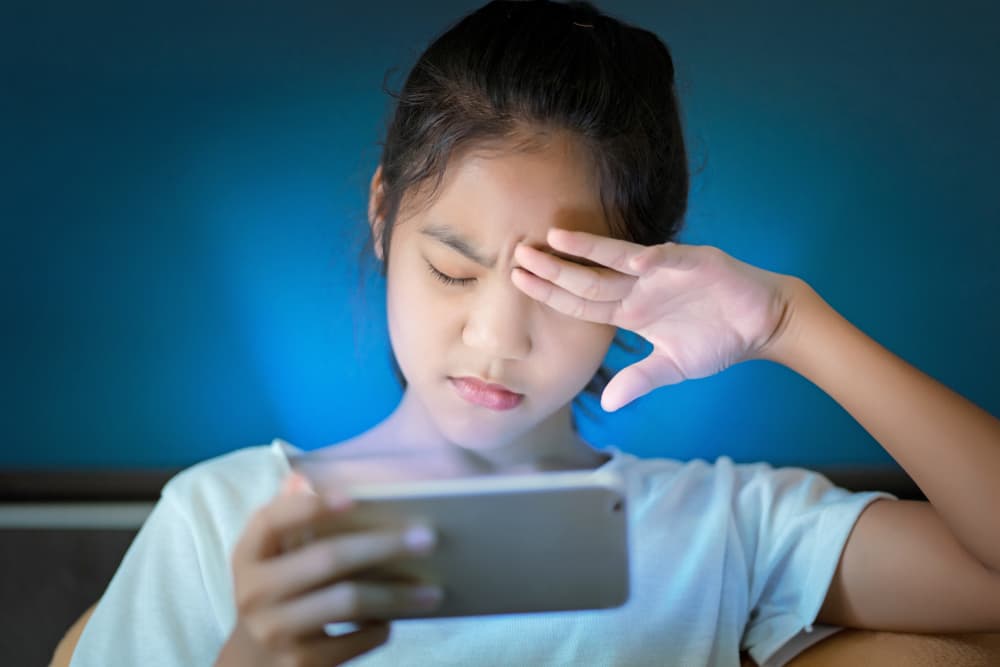 Young girl rubbing her eyes due to digital eye strain from tablet screen blue light exposure